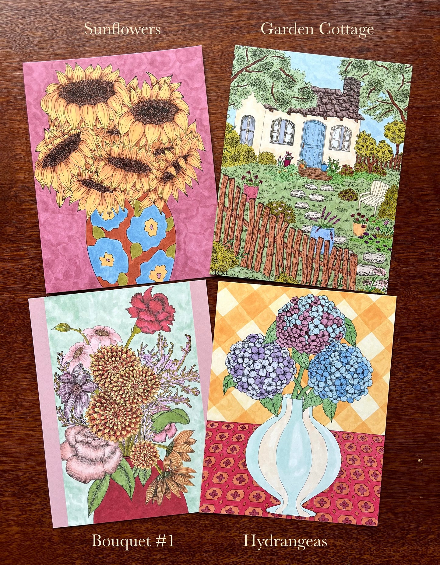 Four greeting cards with sunflowers, garden cottage, bouquet, and hydrangeas on a wooden surface.