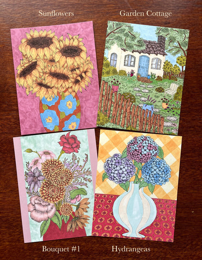 Four greeting cards with sunflowers, garden cottage, bouquet, and hydrangeas on a wooden surface.